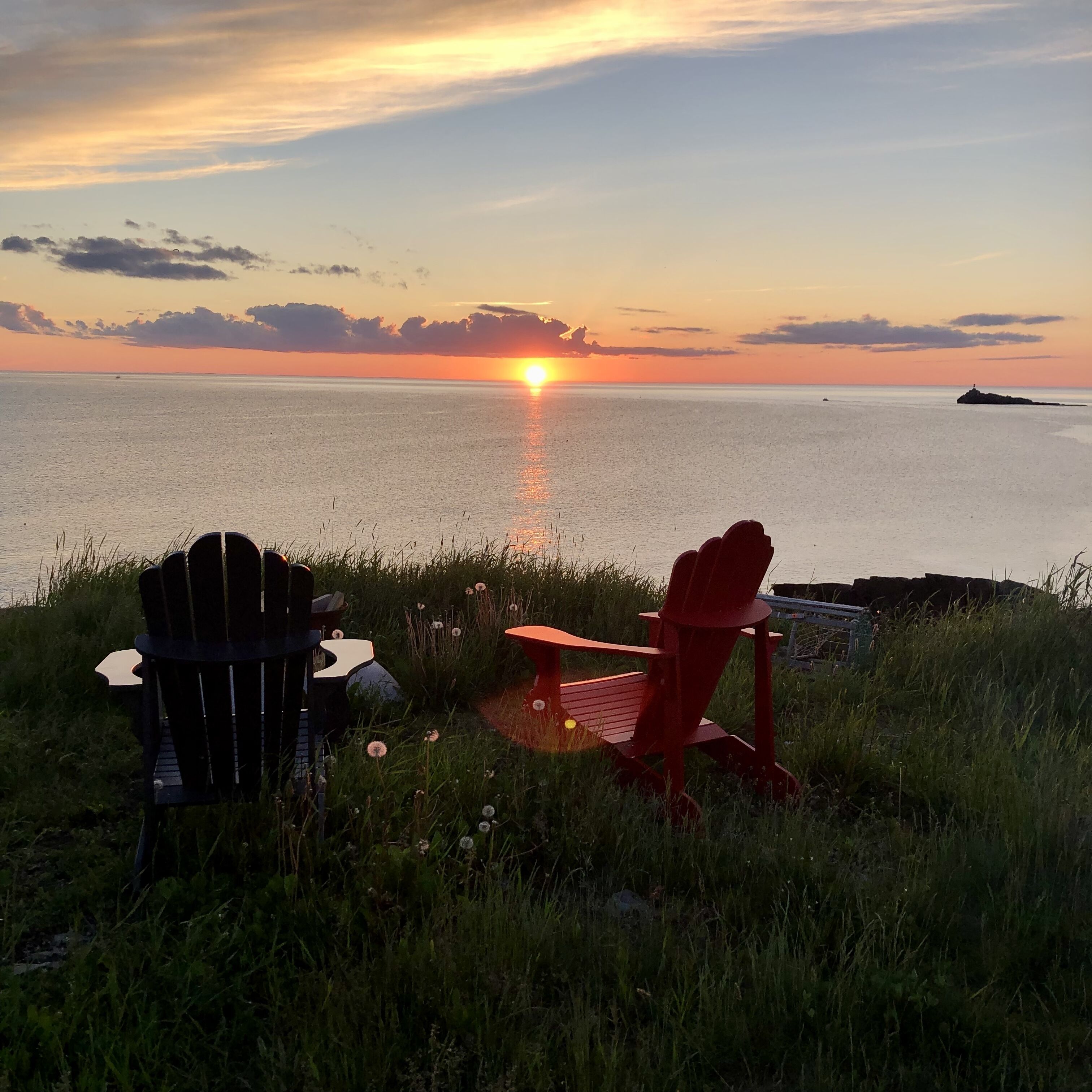 A sunset view with two Adirondack chairs facing a body of water.