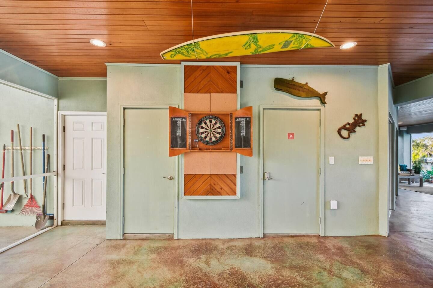 Une pièce avec un jeu de fléchettes, deux portes et une décoration représentant une planche de surf au plafond.