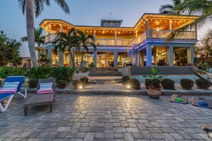 Una casa de dos pisos con un porche cubierto, mobiliario exterior y una escalera que conduce a la entrada.