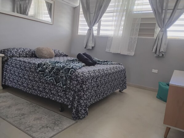 Un dormitorio con cama, mesita de noche, espejo y ventana con cortinas.