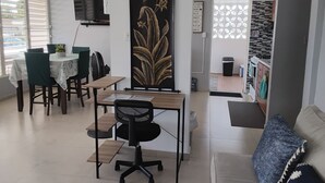 A dining area with a table, chairs, a decorative panel, a television, and a kitchen in the background.