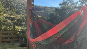 A hammock under a wooden pergola with a view of a hilly landscape.