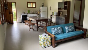 A spacious living area with a wooden sofa, a dining table, and a kitchen area with cabinets and a refrigerator.