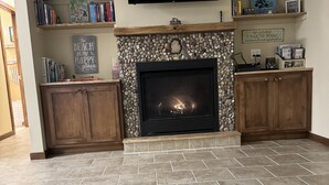 A living room with a fireplace, bookshelves, and a flat-screen TV. - Sweet Retreat West..sandy ORV's and memories made here (Mears)