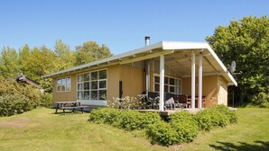 Yhden kerroksen talo, jossa on katettu kuisti, suuret ikkunat ja savupiippu.