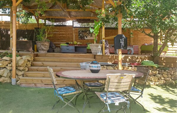 A covered patio area with a round table and chairs, a stone wall, and a wooden deck with steps leading to a seating area. - 5 bedroom lovely home in Rians (Rians)