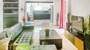 A living room with a sofa, a coffee table, a TV, and a kitchen in the background. - 5 bedroom lovely home in Rians (Rians)