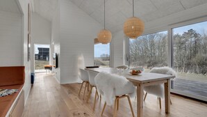 A modern dining area with a wooden table and chairs, large windows, and a view of the outdoors. - Stunning home in Samsø with sauna (Samsø)