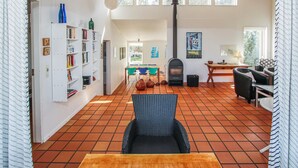 Una zona d'estar àmplia amb terra de rajola, una llar de foc, una taula de dinar amb cadires, una biblioteca i una finestra gran que deixa entrar llum natural.