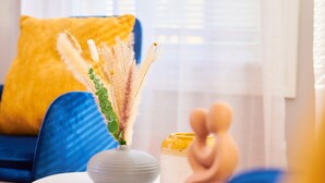 A room with a blue sofa, a white table with a vase of pampas grass, and a yellow pillow. - Cozy apartment 1st 10min Walk Downtown | City View (Providence)