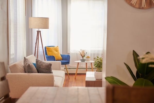 Una sala de estar con un sofá, una silla azul, una lámpara de pie y una pequeña mesa con una planta.