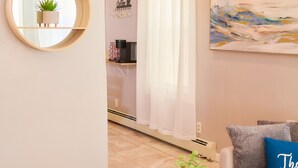 A modern living room with a round mirror, a coffee table with a plant, a sofa with a blue pillow, and a painting on the wall. - Cozy apartment 1st 10min Walk Downtown | City View (Providence)