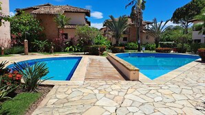 Zona de piscina con suelo de piedra, rodeada de abundante vegetación y un edificio con techo de tejas.