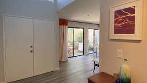 Une pièce spacieuse dotée d’une grande porte-fenêtre coulissante donnant sur un espace extérieur, d’un meuble en bois orné d’objets décoratifs et d’un tableau abstrait encadré accroché au mur.