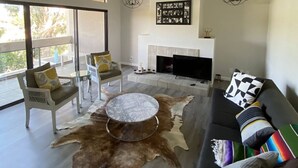 Un salon spacieux doté d’un ventilateur de plafond, d’une cheminée, d’un grand téléviseur et d’un tapis en peau de vache.