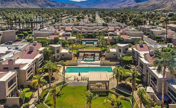 Relax by the central pool surrounded by lush lawns and palm trees, with scenic views from multiple levels.