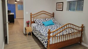 Een slaapkamer met een houten bed, een klein nachtkastje, een inlijsting foto aan de muur en een raam met zonwering.