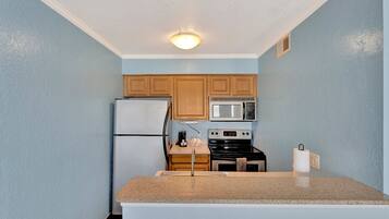 A kitchen with light blue walls, wooden cabinets, a white refrigerator, a microwave, a stove, and a granite countertop.