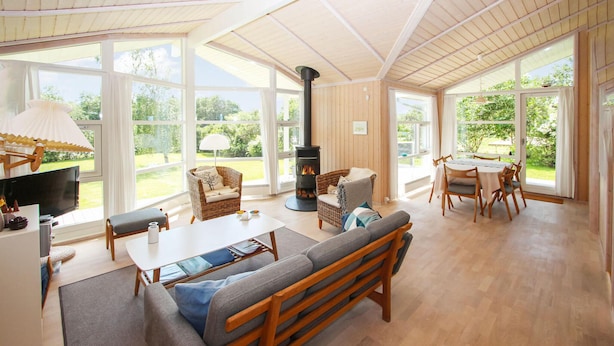 A spacious living room with a large fireplace, comfortable seating, and large windows offering a view of the outdoors. - 3 bedroom beautiful home in Samsø (Samsø)
