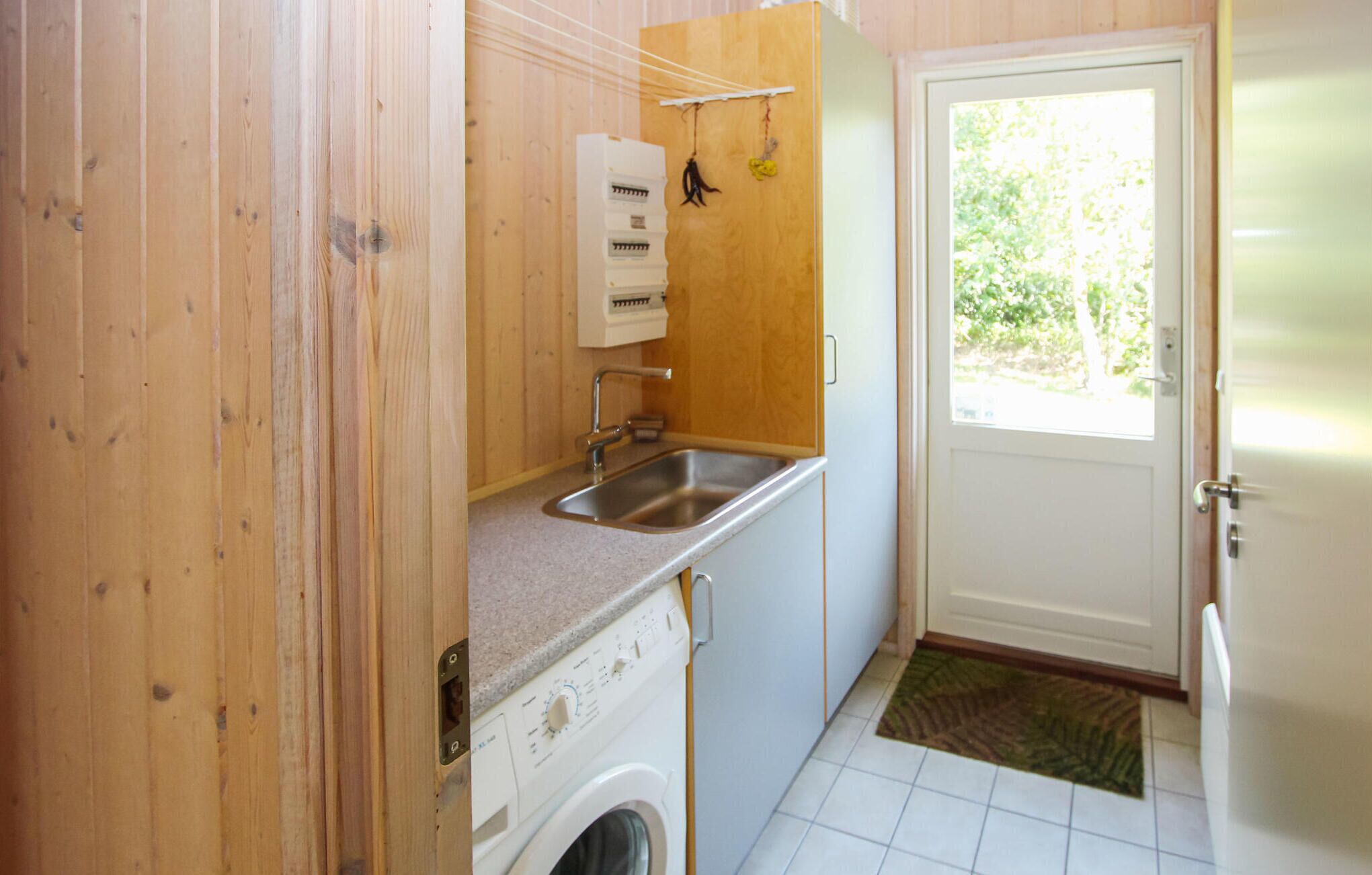 A compact kitchen with a washing machine, a sink, and a window with a view of greenery.