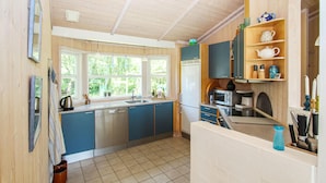 A compact kitchen with blue cabinets, a dishwasher, a refrigerator, and a microwave. There are windows providing natural light and a view of greenery outside. - 3 bedroom beautiful home in Samsø (Samsø)