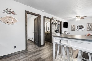 Una cocina moderna con piso de madera, una barra blanca y un ventilador de techo.