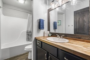 Une salle de bain avec un meuble-lavabo en bois, un lavabo blanc, un grand miroir et un espace douche.