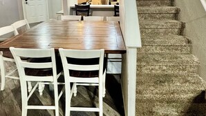 Ein Essbereich mit Holztisch und weißen Stühlen, eine Treppe mit Teppichstufen und ein Deckenventilator.