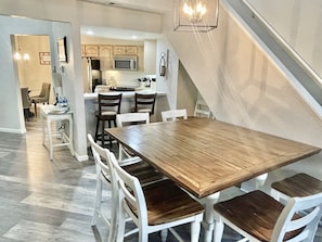 Une cuisine moderne avec des meubles en bois, un four à micro-ondes et un coin repas comprenant une table en bois et des chaises blanches.