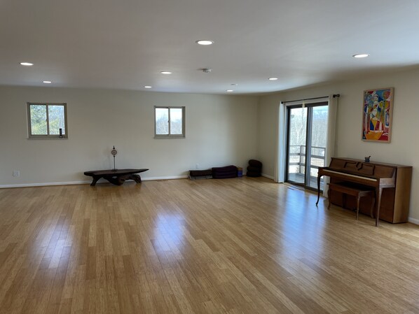 A spacious room with hardwood flooring, a piano, a bench, and two windows.