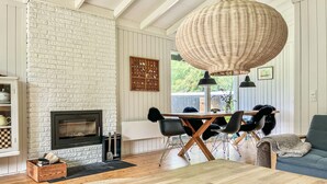 A living room with a fireplace, wooden flooring, a dining table with chairs, and a large woven light fixture. - Nice home in Tisvildeleje with WiFi (Tisvildeleje)