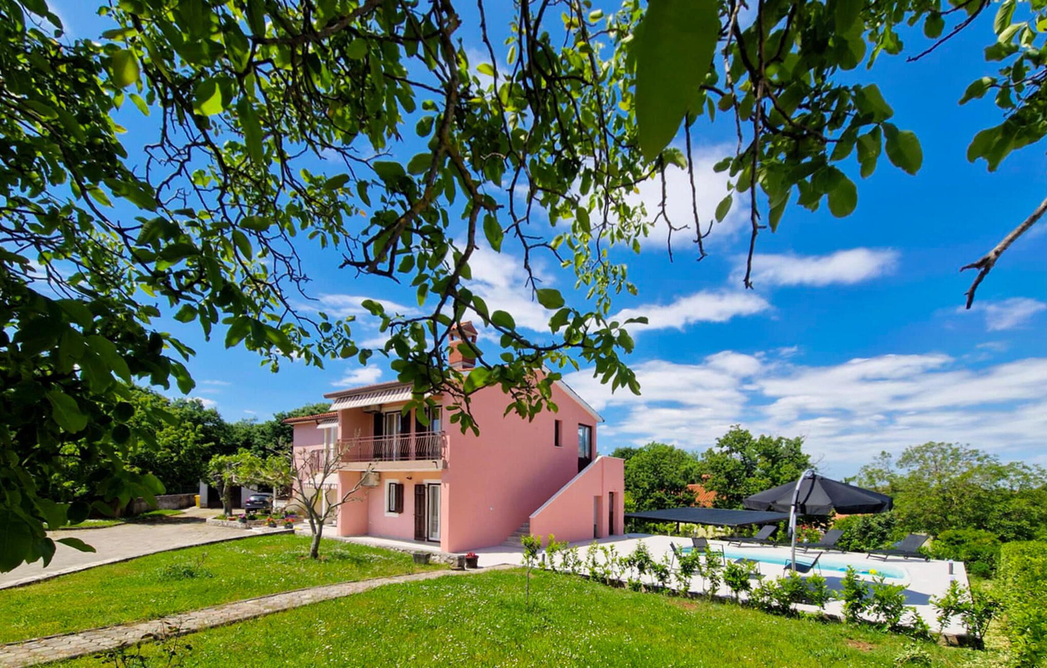 A pink two-story house with a balcony, a swimming pool, and a garden.