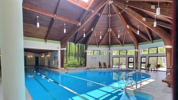 An indoor swimming pool with clear lanes, wooden beams, and a view of greenery outside. - Red Bear Inn- 6.5 Baths! Grill, Pool, Central (Killington)