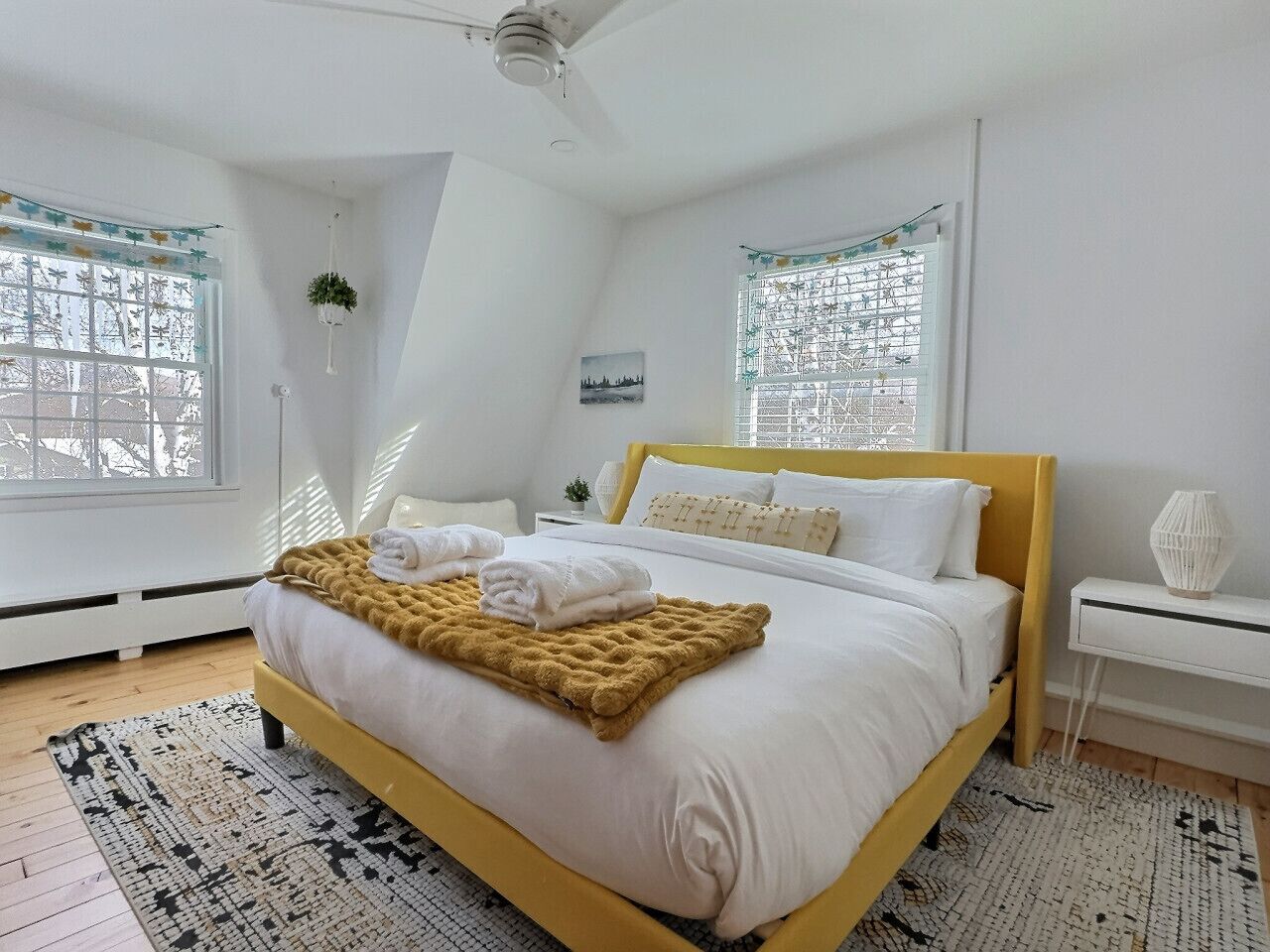 Ein Schlafzimmer mit einem Bett, einem Nachttisch, einem Fenster und einem Deckenventilator.
