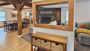 A living room with a stone fireplace, wooden beams, a large mirror, and a gray sofa. - Red Bear Inn- 6.5 Baths! Grill, Pool, Central (Killington)