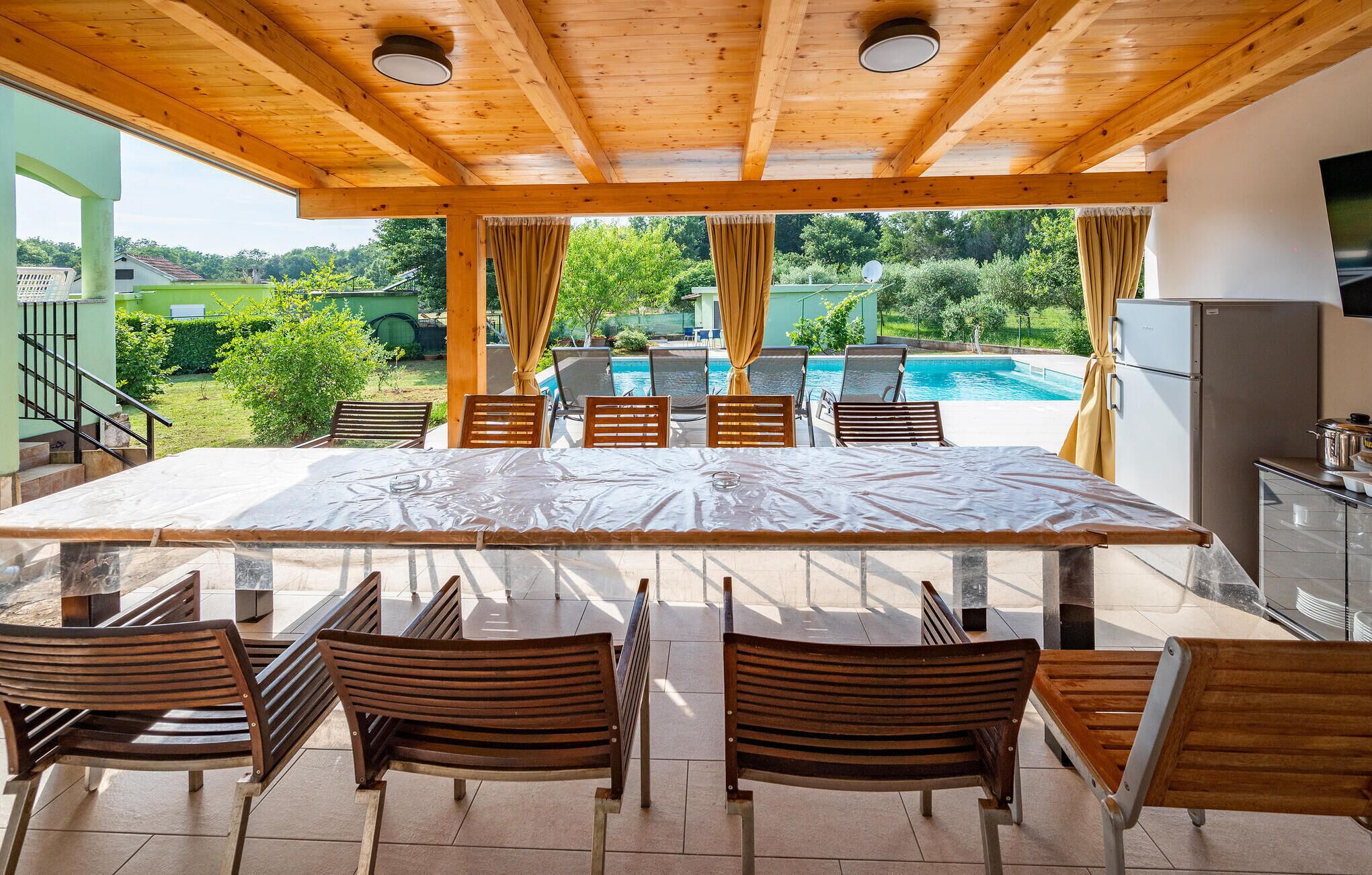 A covered outdoor dining area with a pool view, wooden chairs, and a table.