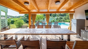 Un área de comedor al aire libre techada con vista a la piscina, sillas de madera y una mesa.