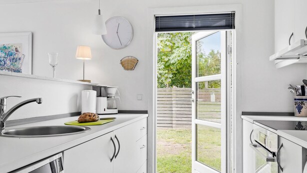 A modern kitchen with white cabinets, a sink, a coffee maker, and a window with a view of a garden. - Lovely home in Samsø with WiFi (Samsø)