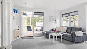 A modern living room with a grey sofa, a coffee table, and a sliding glass door leading to an outdoor seating area. - Lovely home in Samsø with WiFi (Samsø)