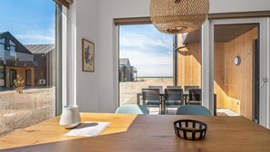Een moderne eethoek met een houten tafel, stoelen en een pendellamp van riet. Op de muur hangt een lijst met een kaart van Denemarken.