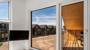 Een modern interieur met een grote schuifglazen deur die uitkomt op een terras met uitzicht op een complex aan de kust.