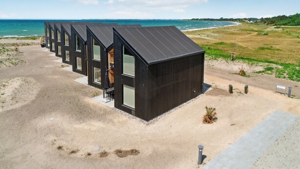 Een rij moderne, donkere cabins met grote ramen, gelegen aan een zandstrand met uitzicht op de oceaan.