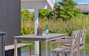 A wooden outdoor seating area with a table and chairs, a bottle, and a glass. - Beautiful home in Hjørring with WiFi (Hjørring)