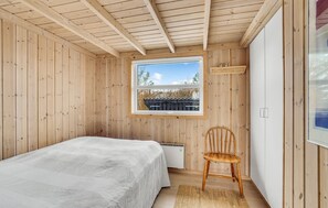 A bedroom with a bed, a chair, a window, and wooden walls. - Beautiful home in Hjørring with WiFi (Hjørring)