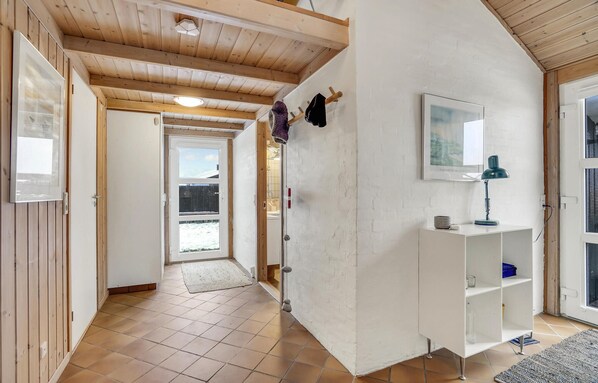 A hallway with wooden beams, a white wall, a framed picture, and a white cabinet with a lamp.