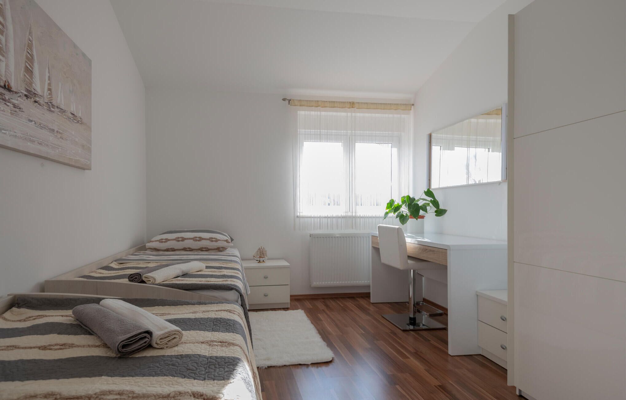 A bedroom with a bed, bedside table, dresser, and a large window with curtains.