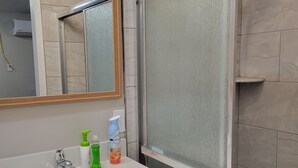 Une salle de bain avec un lavabo blanc, un miroir, un espace douche et des articles de toilette posés sur le comptoir.
