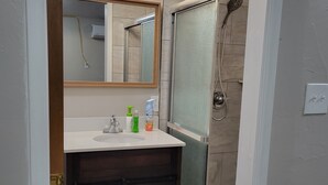 Une salle de bain avec un meuble-lavabo en bois, un miroir, une cabine de douche et des toilettes.