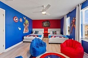 Una habitación con dos camas, un ventilador de techo y un mural en la pared con motivos rojos y azules.