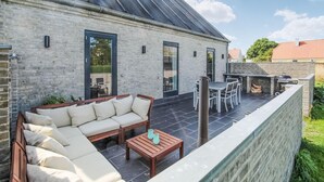 A modern outdoor patio with a brick wall, a sofa, a table, and a grill area. - Beautiful home in Samsø with WiFi (Samsø)